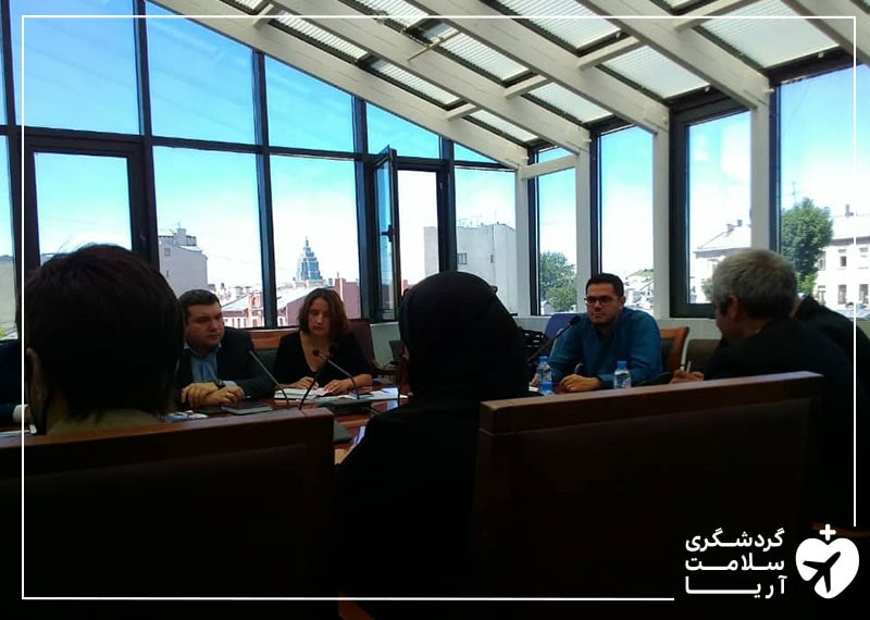 محمد نصری و تعدادی خانم و آقا در یک اتاق با پنجره های زیاد، دور یک میز جلسه برگزار کرده اند و در حال مذاکره هستند