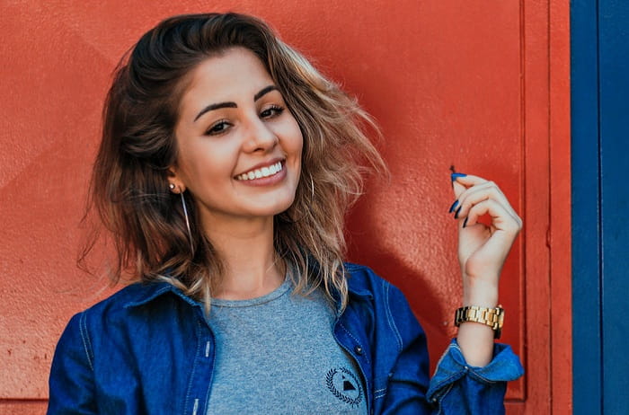 a girl with brown hair standing in front of the camera and smiling with her crowned teeth