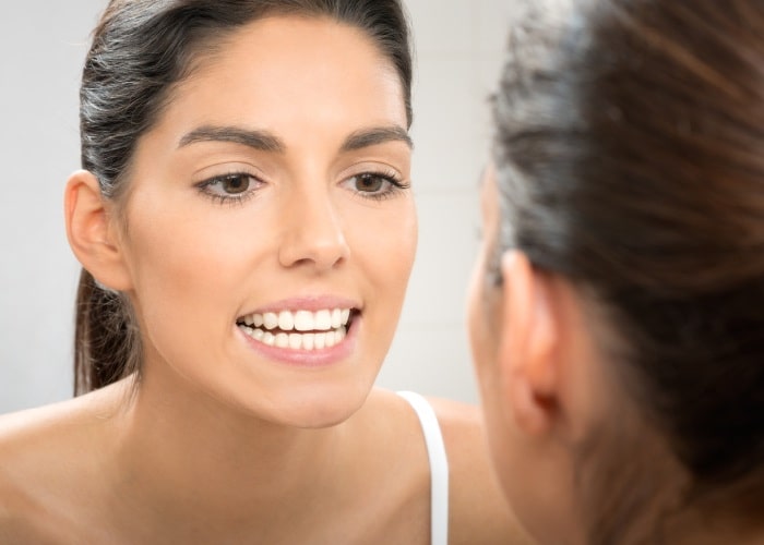 woman showing her white teeth in the mirror after getting porcelain veneers in iran