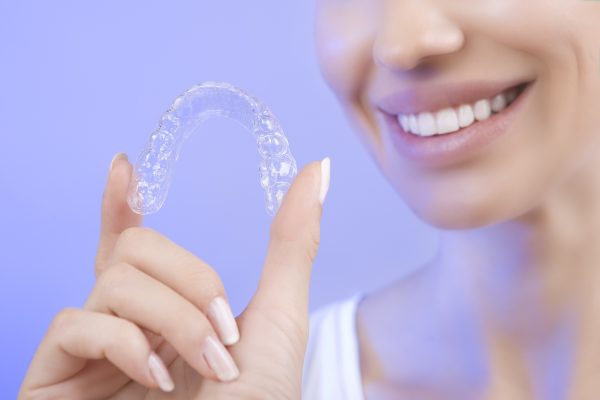 woman holding clear aligners with her hand while smiling