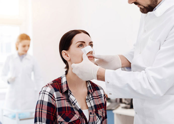 doctor taping a woman's nose after nose surgery