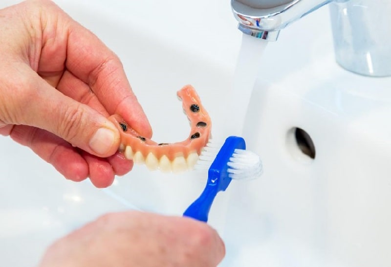 denture being brushed over a sink