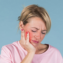 blonde adult woman suffering from denture pain while putting her hand on her cheek and teeth