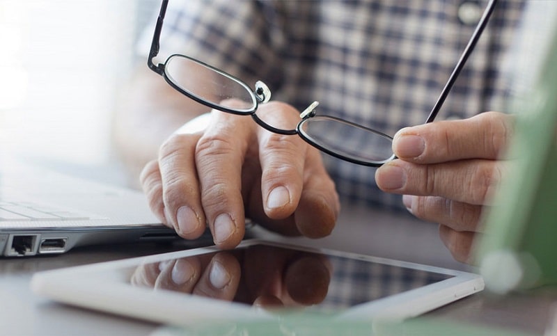 man working with a tablet while holding his eyeglasses in hand