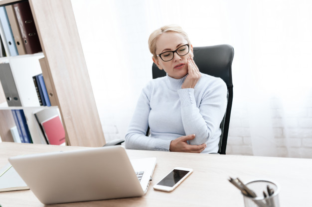 woman in her office suffering from toothache and massaging her teeth