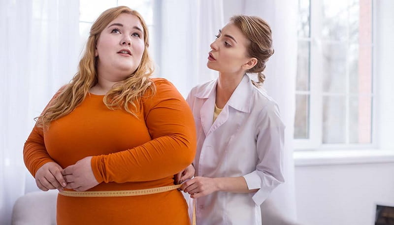 doctor measuring the waistline of an obese woman with large breasts