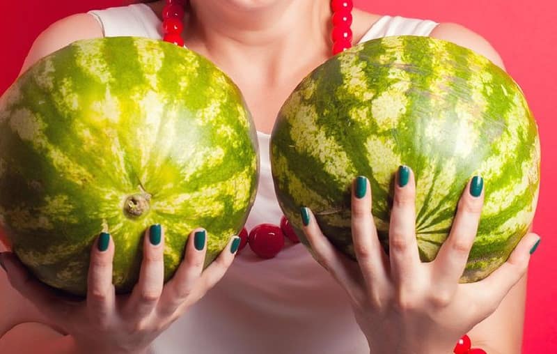 woman holding two watermelons in front of her chest, signifying too large breasts