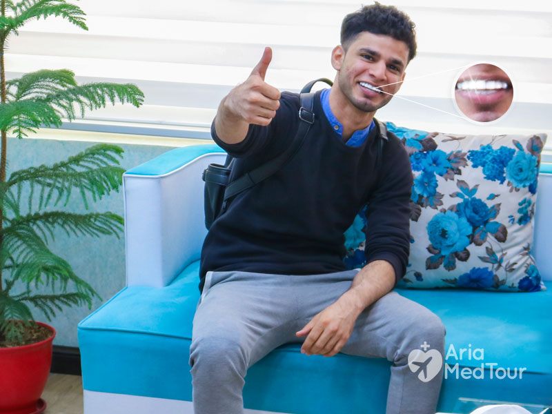 smiling man sitting on sofa in AriaMedTour office showing a thumbs up gesture after dental veneers procedure in Iran