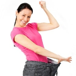 young woman with in pink T shirt happily showing her jeans' loose waist after weight loss