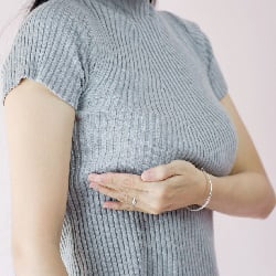 woman in grey pullover pushing her breasts up with left forearm