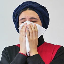 young girl with scarf blowing her nose with facial tissue indication
