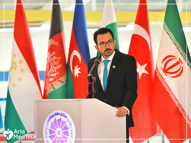 Hadi Shajari giving speech at ECO Confobition with flags of ECO member states seen in the background