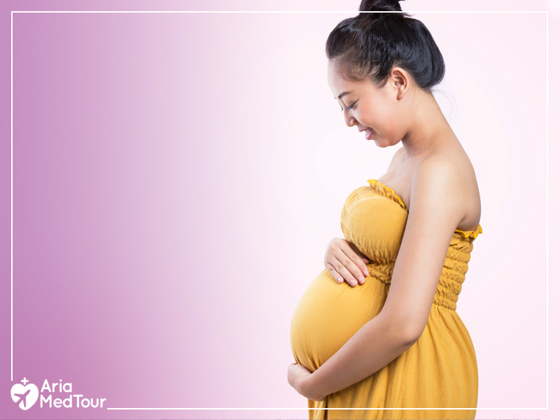 Chinese pregnant woman with a yellow dress while she is touching her belly 