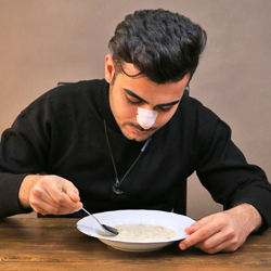 boy with a black shirt and splint on his nose eating soup